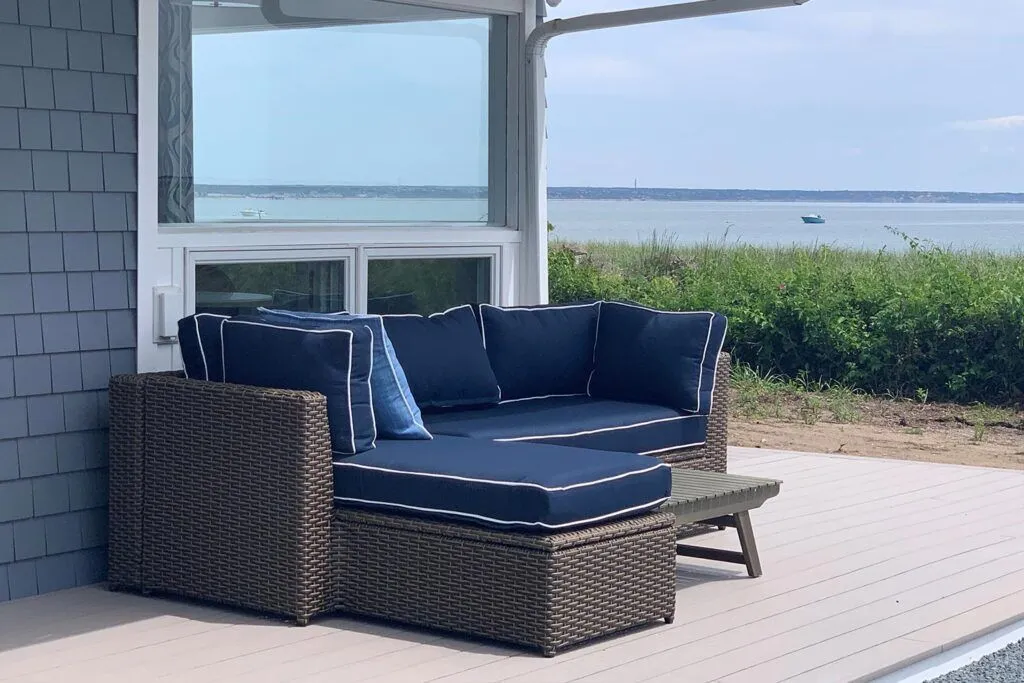A wicker sofa with blue cushions sits on a deck overlooking the water.