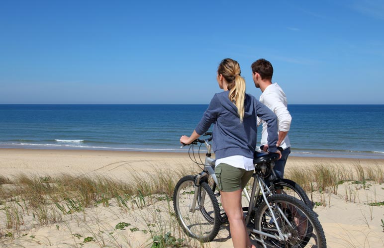 A bicycling couple looking over the beach.