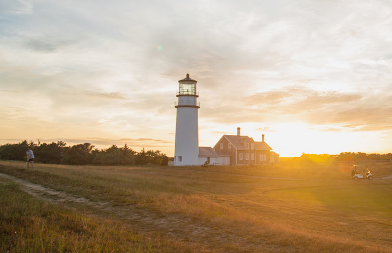 Golfer in the foreground and lighthouse in the background, at sunset